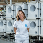 Trabajadora de Balay en una fábrica de electrodomésticos, con módulos de lavadoras apilados en el fondo de la línea de producción